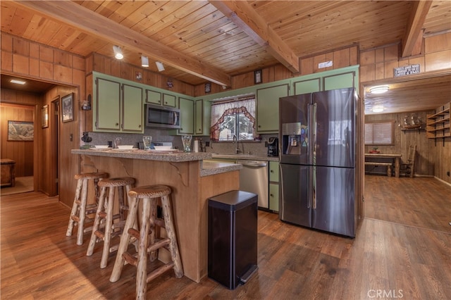 kitchen with wooden walls, green cabinetry, a peninsula, stainless steel appliances, and beam ceiling