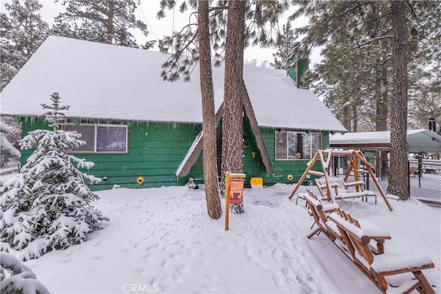 snow covered rear of property featuring a playground and fence