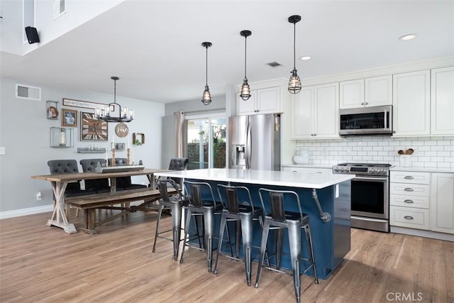 kitchen featuring visible vents, backsplash, a kitchen island, light countertops, and appliances with stainless steel finishes