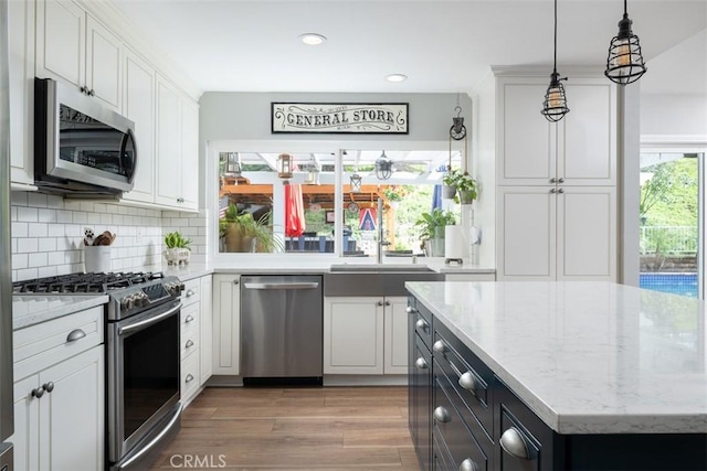 kitchen featuring backsplash, wood finished floors, white cabinets, stainless steel appliances, and a sink