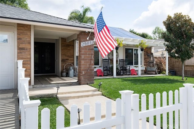 doorway to property featuring a lawn, roof mounted solar panels, a porch, fence, and roof with shingles