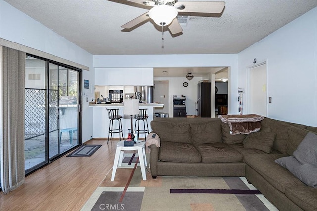 living area with ceiling fan, a textured ceiling, and light wood finished floors