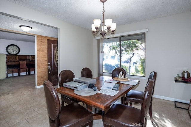 dining room with a textured ceiling, light tile patterned flooring, wood walls, baseboards, and an inviting chandelier