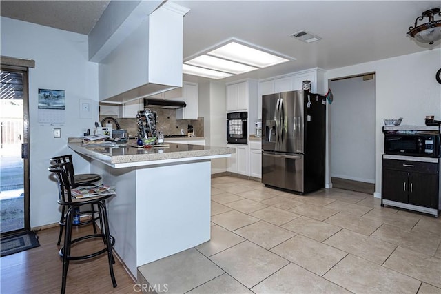 kitchen featuring visible vents, backsplash, white cabinets, a peninsula, and black appliances