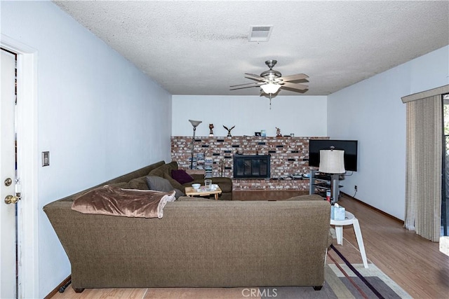 living area with a textured ceiling, ceiling fan, a fireplace, and wood finished floors