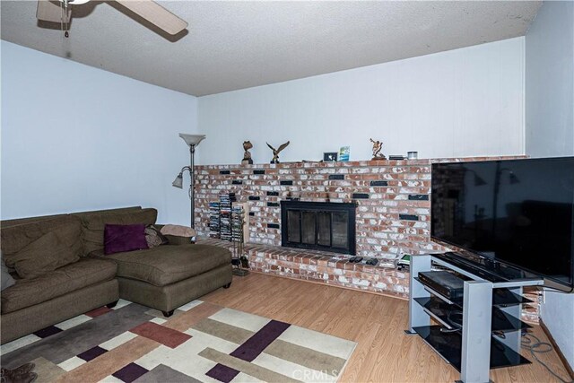 living area featuring a textured ceiling, a fireplace, a ceiling fan, and wood finished floors