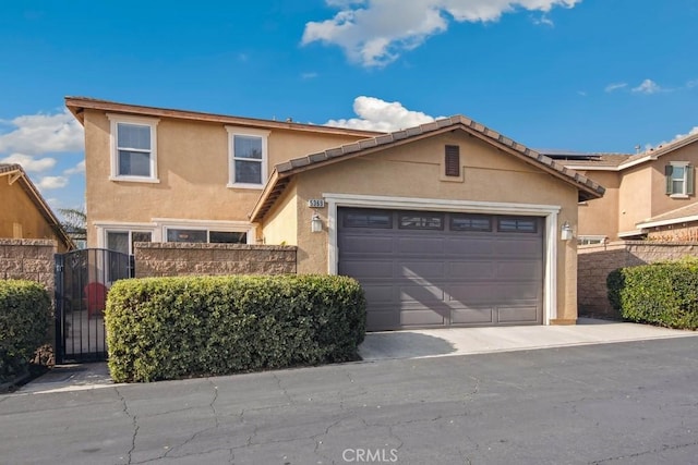 traditional home with an attached garage, a gate, fence, and stucco siding