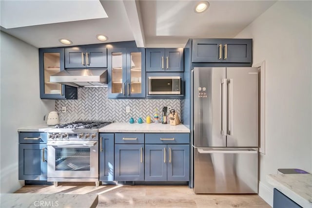 kitchen featuring under cabinet range hood, light wood-style floors, appliances with stainless steel finishes, backsplash, and glass insert cabinets