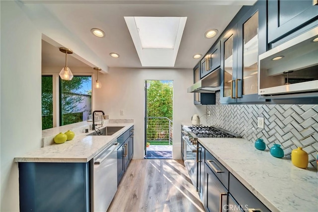 kitchen with light wood finished floors, decorative backsplash, stainless steel appliances, under cabinet range hood, and a sink