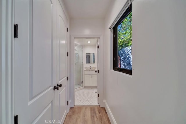 corridor with light wood finished floors, baseboards, and a sink