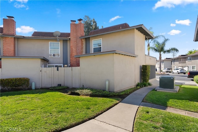 view of property exterior featuring a yard, fence, a chimney, and stucco siding