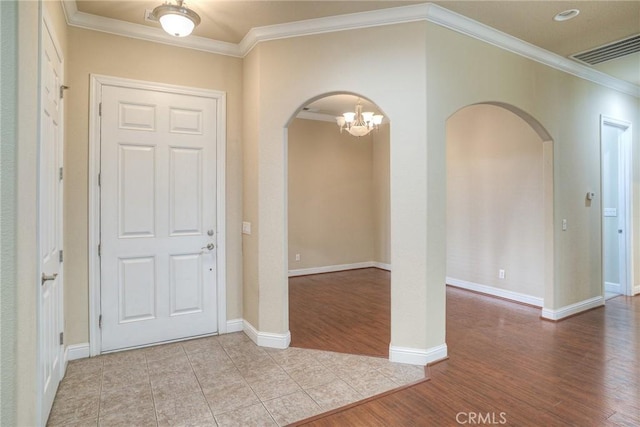 foyer entrance featuring baseboards, visible vents, arched walkways, light wood-style flooring, and crown molding