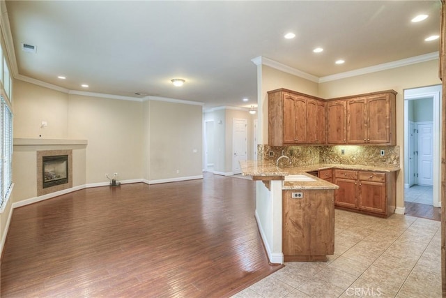 kitchen featuring a fireplace, backsplash, open floor plan, a sink, and a peninsula