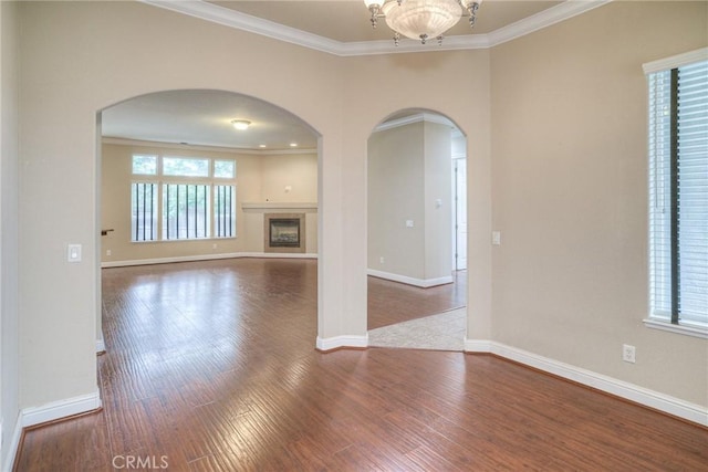 unfurnished living room with arched walkways, crown molding, baseboards, and wood finished floors