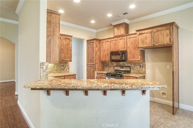 kitchen with arched walkways, black microwave, a peninsula, visible vents, and stainless steel gas stove