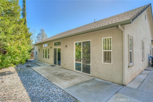 rear view of property featuring a patio, a shingled roof, and stucco siding