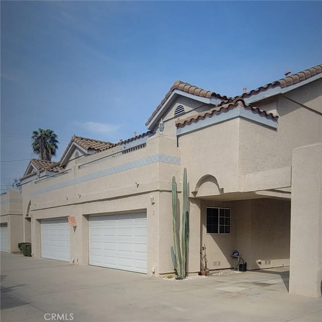 exterior space with stucco siding, concrete driveway, an attached garage, and a tile roof