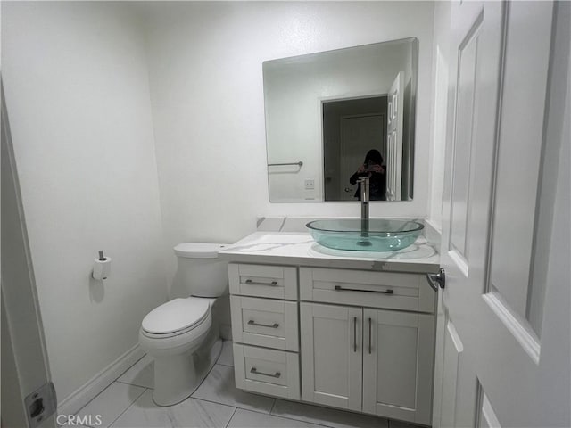 half bathroom with baseboards, toilet, and vanity