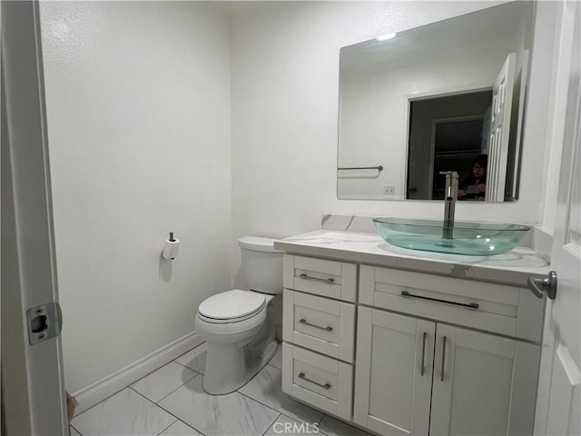 half bathroom with vanity, toilet, and baseboards