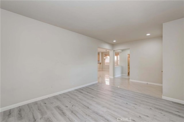 spare room featuring a notable chandelier, baseboards, wood finished floors, and recessed lighting