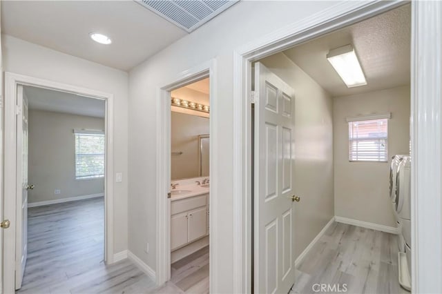 corridor with a healthy amount of sunlight, light wood-style flooring, visible vents, and washer and dryer