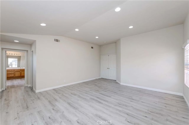 unfurnished room with visible vents, vaulted ceiling, light wood-style flooring, and baseboards