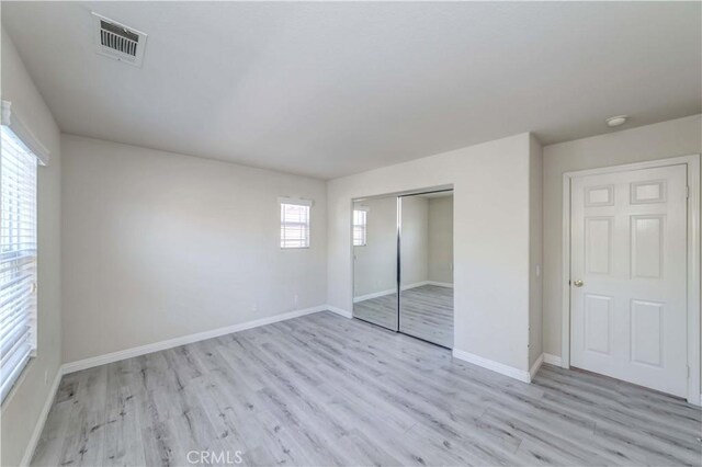 unfurnished bedroom with light wood-style floors, a closet, visible vents, and baseboards