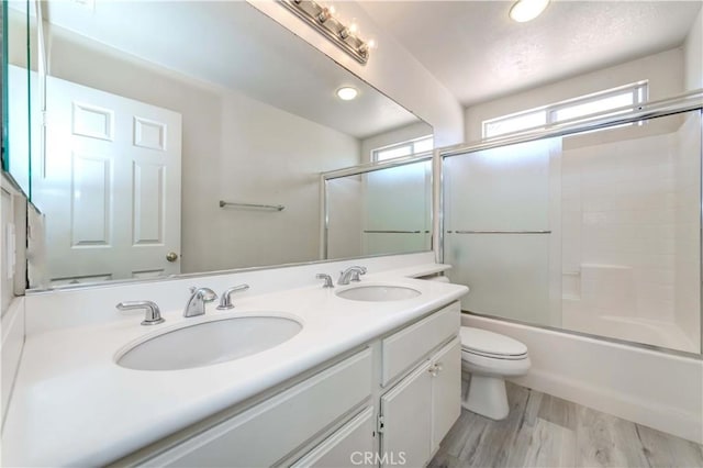 full bath with double vanity, a sink, toilet, and wood finished floors