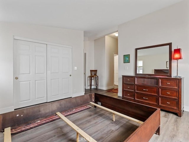 bedroom with light wood-type flooring, a closet, and baseboards