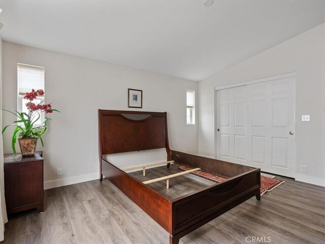 bedroom with lofted ceiling, a closet, baseboards, and wood finished floors