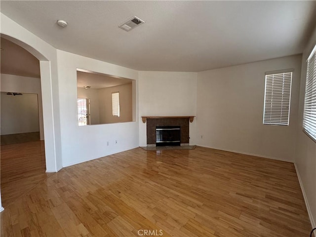 unfurnished living room featuring baseboards, visible vents, arched walkways, light wood-style floors, and a fireplace