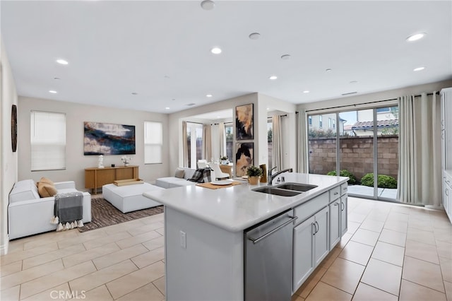 kitchen with light tile patterned floors, light countertops, open floor plan, a sink, and dishwasher