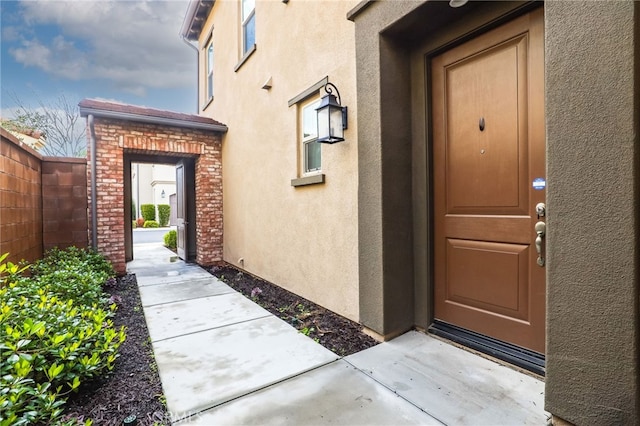 view of exterior entry featuring fence and stucco siding