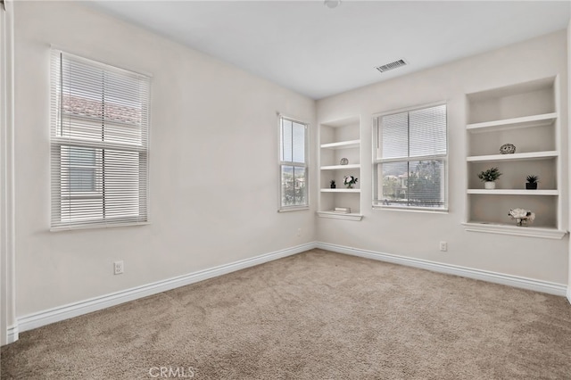 spare room with carpet floors, built in shelves, visible vents, and baseboards