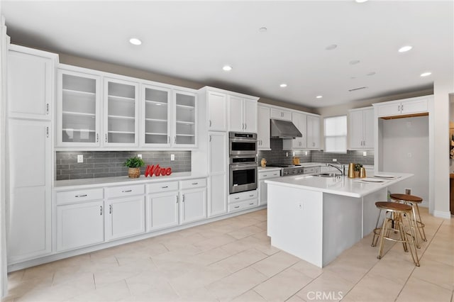 kitchen with double oven, glass insert cabinets, white cabinets, a sink, and under cabinet range hood