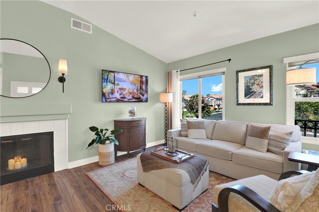 living area with wood finished floors, baseboards, visible vents, lofted ceiling, and a tile fireplace