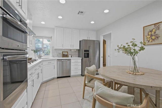 kitchen with light tile patterned floors, appliances with stainless steel finishes, light countertops, white cabinetry, and a sink