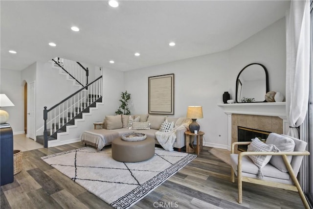 living room with recessed lighting, wood finished floors, a tiled fireplace, and stairs