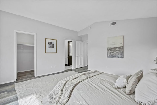 bedroom featuring lofted ceiling, visible vents, a spacious closet, wood finished floors, and baseboards