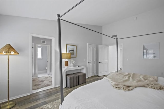 bedroom with lofted ceiling, visible vents, ensuite bath, and wood finished floors