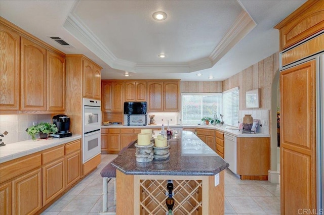 kitchen with a raised ceiling, white appliances, a kitchen island, and light tile patterned floors