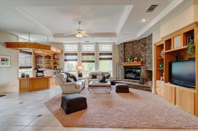 living area with a fireplace, visible vents, a tray ceiling, and ornamental molding