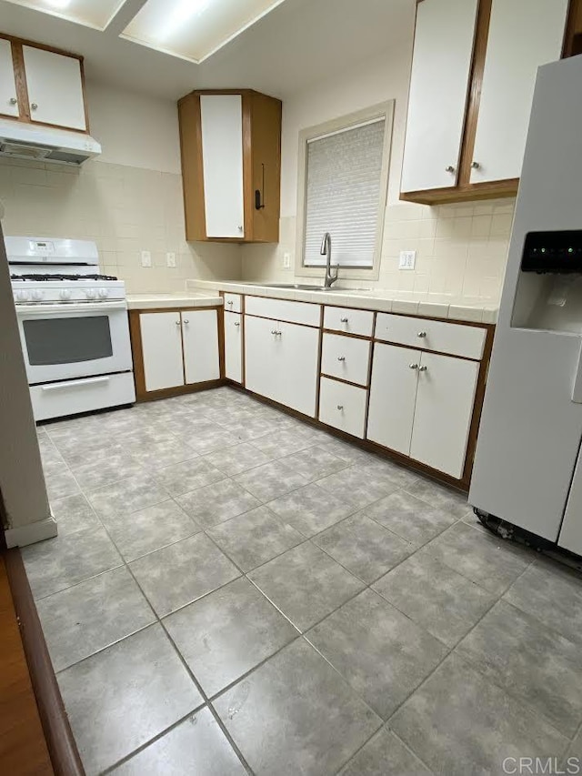 kitchen featuring backsplash, white cabinetry, a sink, white appliances, and under cabinet range hood