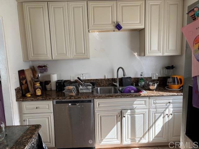 kitchen with stainless steel dishwasher, dark stone countertops, and a sink