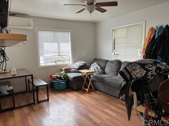 living area featuring a ceiling fan, a wall unit AC, and wood finished floors