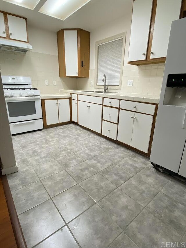 4169 Central Ave, San Diego, CA 92105 - kitchen featuring white appliances, a sink, under cabinet range hood, white cabinets, and backsplash