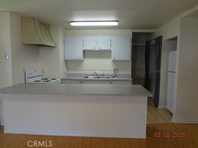 kitchen featuring a peninsula, white appliances, a sink, light countertops, and custom exhaust hood