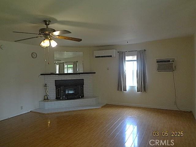 unfurnished living room with ceiling fan, wood finished floors, an AC wall unit, a brick fireplace, and a wall mounted air conditioner