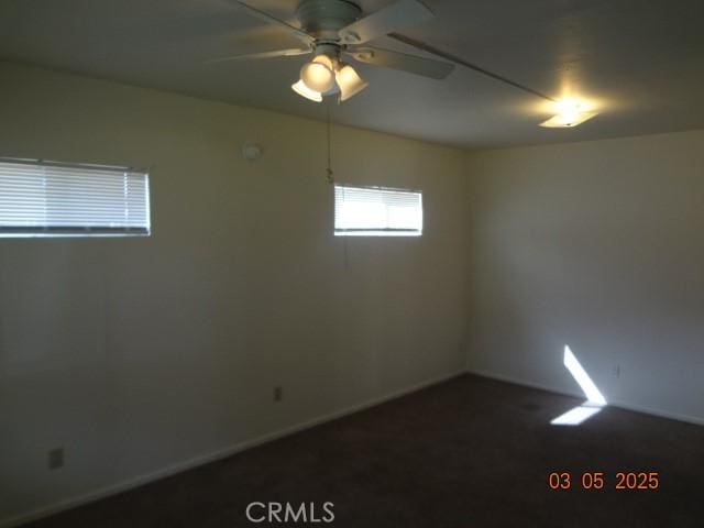 unfurnished room featuring baseboards, dark colored carpet, and a ceiling fan