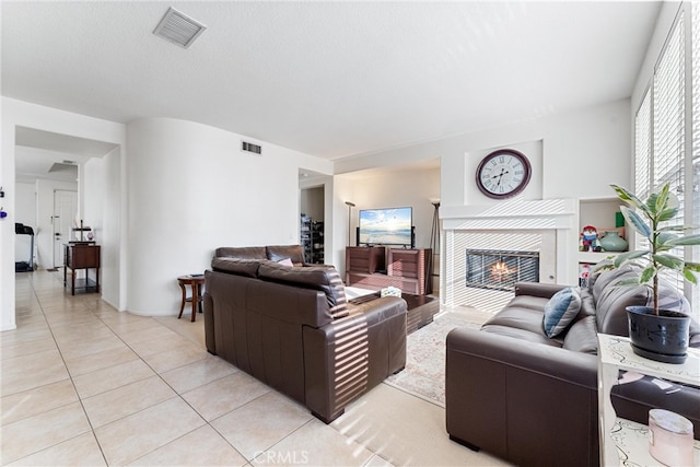 living room featuring light tile patterned floors, visible vents, a textured ceiling, and a fireplace